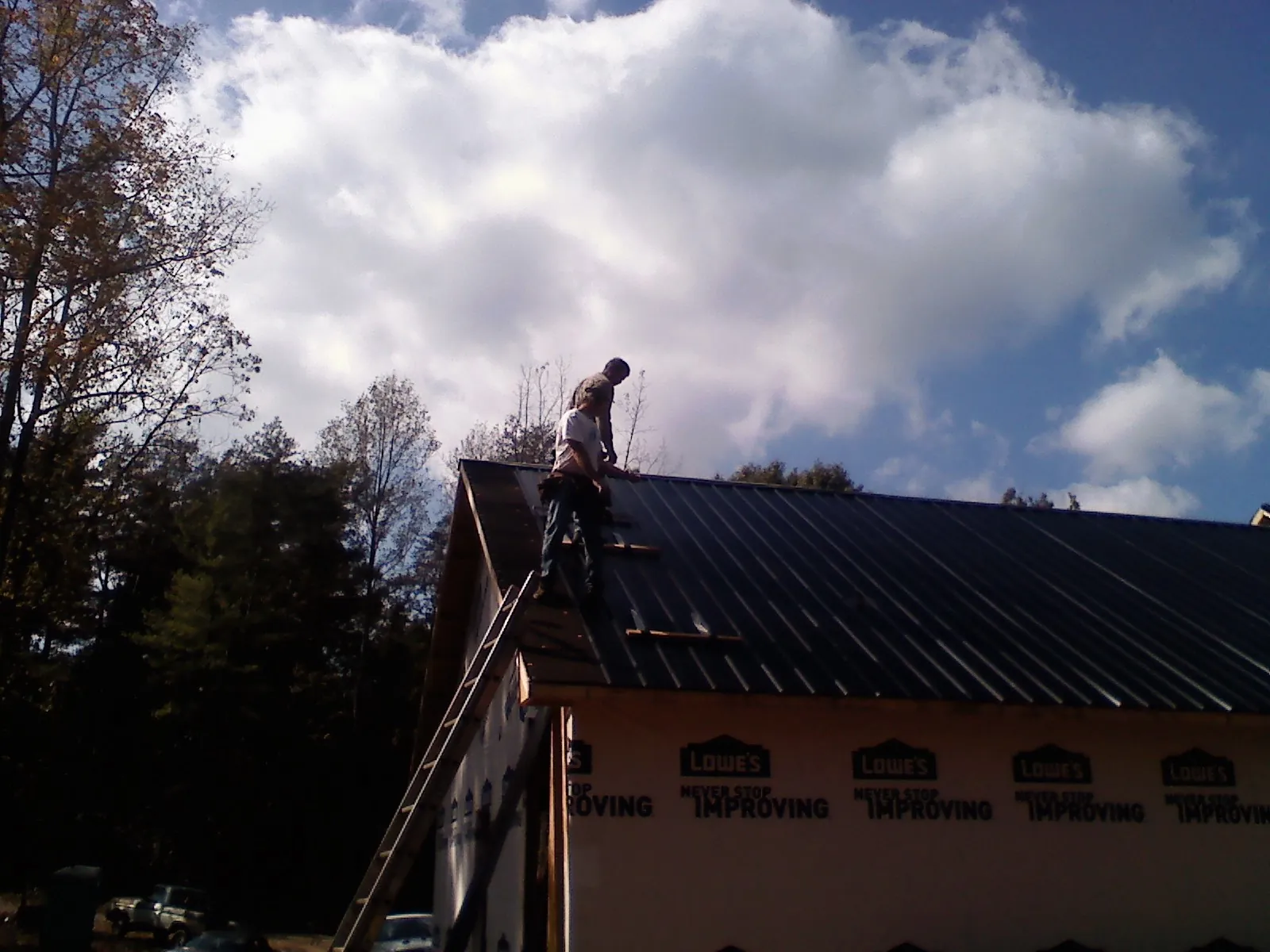 Roofer fastening dark metal panels high against a cloudy sky, from a Roof Inspection job in Foley