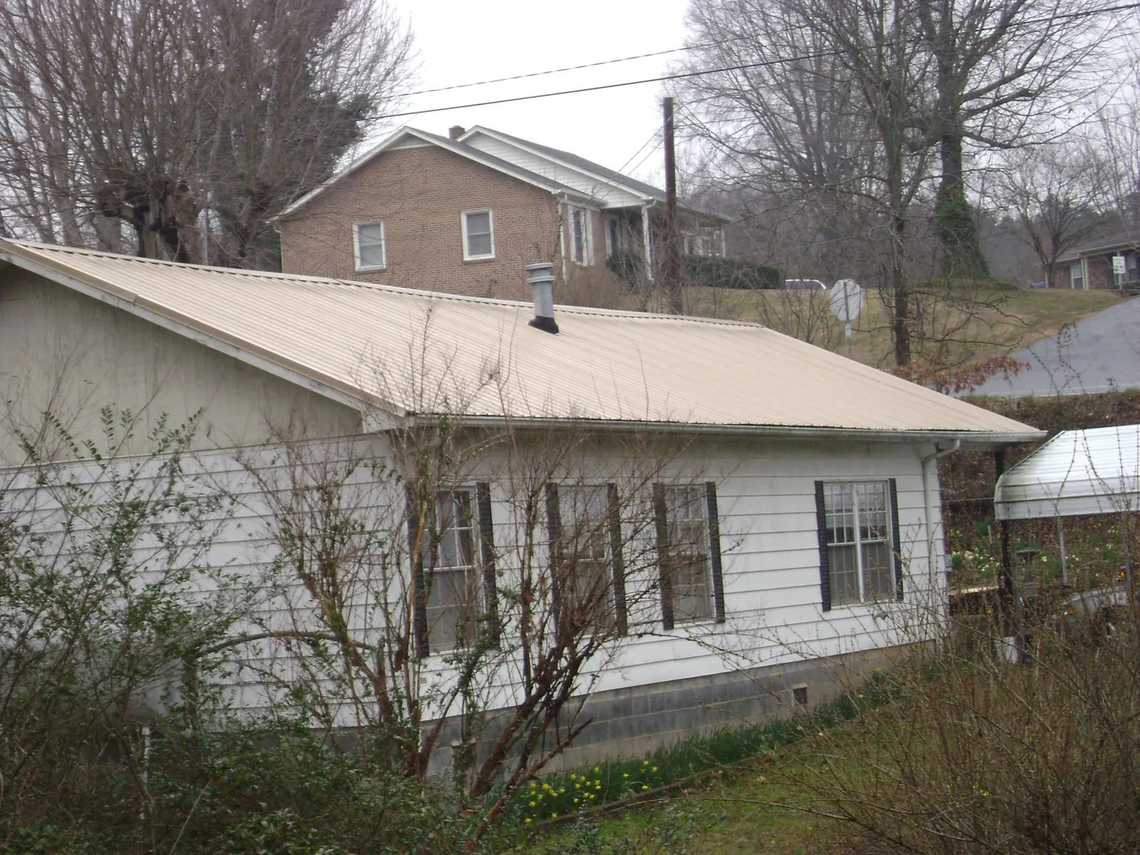 Tan metal roof on a white sided house set into a hillside — Commercial Roofing by Roofing Brothers in Foley